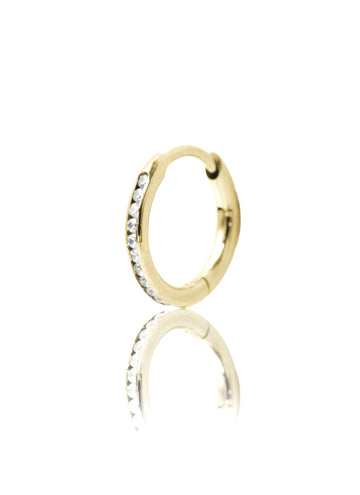 Złoty kolczyk w kształcie koła z cyrkoniami na jasnym tle